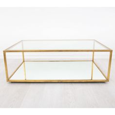 a glass and brass coffee table with mirrored shelves on the bottom, in front of a white wall