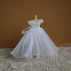 a white wedding dress is sitting on a lace tablecloth with a mannequin