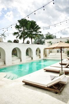 an outdoor pool with lounge chairs and umbrellas next to the swimming pool at dusk