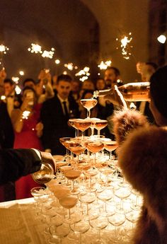 many people are holding wine glasses with sparklers in the air as they sit at a table full of champagne flutes