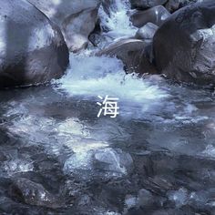 there is a small white sign in the middle of some water and rocks with writing on it