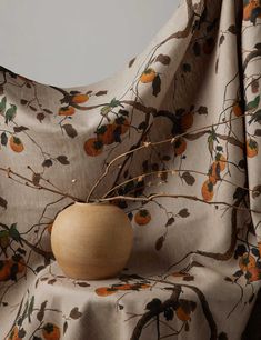 a wooden vase sitting on top of a table covered in a fabric with oranges and leaves