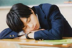 a young man is asleep on his desk with his head resting on his hands and eyes closed