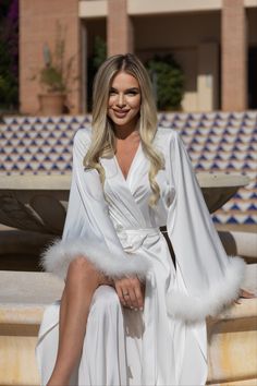 a woman sitting on top of a fountain wearing a white robe and fur stoler