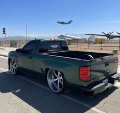 a green truck is parked on the side of the road near an air plane in the background