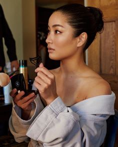 a woman in a bathrobe looking at her cell phone while she is getting ready to brush her hair