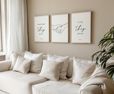 a living room with white couches and paintings on the wall above them, along with a potted plant