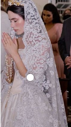 a woman in a white wedding dress and veil with her hands clasped to her chest