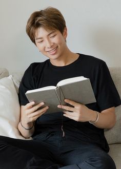 a man sitting on a couch reading a book with headphones in his ears and smiling at the camera