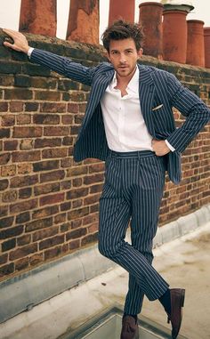 a man in a suit leaning against a brick wall