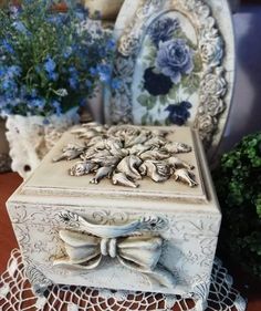 a white box sitting on top of a doily next to some blue and white flowers