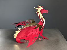 a paper sculpture of a red dragon sitting on a metal surface with its wings folded