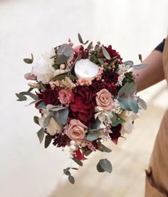 a bridal bouquet with roses and greenery on the bride's hand,