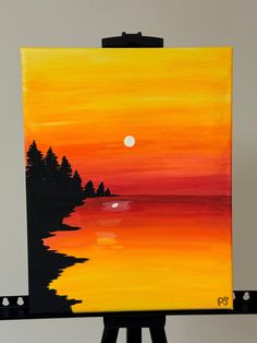 an easel with a painting on it that has a sunset and trees in the water