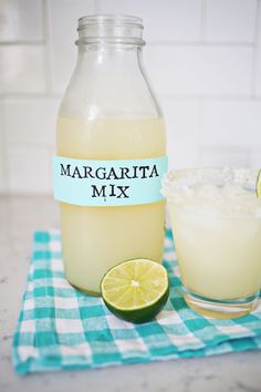 margarita mix in a glass bottle next to a half - eaten lime on a blue and white checkered cloth