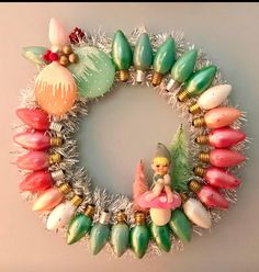 a wreath made out of christmas ornaments and tinsel on the wall with an elf figurine