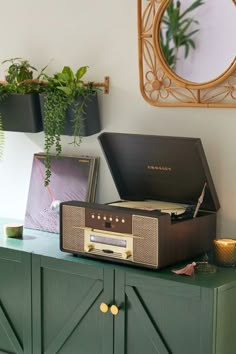 a record player sitting on top of a green cabinet next to a mirror and potted plant