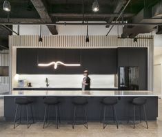 a man standing in front of a kitchen island with stools and lights on it