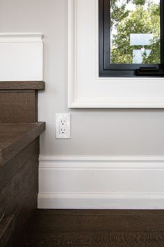 an empty room with white walls and wood flooring on the side, along with a black framed window