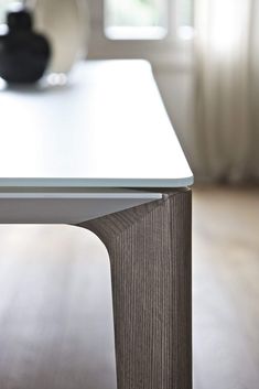 a white table with a black vase sitting on it's side next to a window