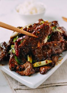 a white plate topped with meat covered in sauce and vegetables next to chopsticks