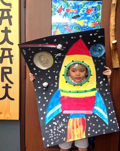 a child holding up a cardboard rocket ship