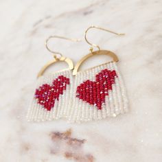 the beaded heart earrings are hanging from gold hoops on a marble countertop