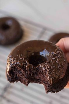 a person holding a chocolate donut with one bite taken out