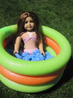 a doll is sitting in an inflatable pool on the grass, with blue balls