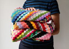 a person holding three crocheted blankets in their hands