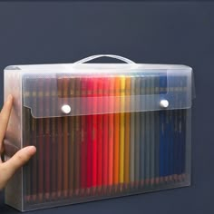 a hand holding a clear box with colored pencils in it