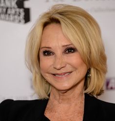 an older woman with blonde hair smiling at the camera and wearing a black blazer