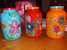 three painted jars sitting on top of a wooden table