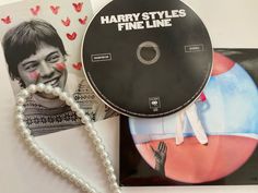 there is a cd and a necklace on the table next to it, which has an image of harry styles