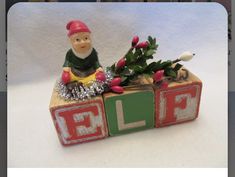 a small wooden block with a gnome sitting on it's top and the letters elf spelled out