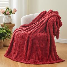 a red blanket sitting on top of a white chair next to a potted plant