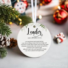 a white ornament with the words leader hanging from it's center surrounded by christmas decorations