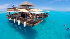 a house boat floating in the ocean with people swimming around and on it's side