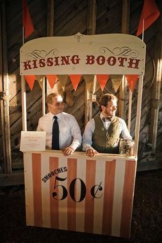 two men are sitting at a booth for kissing booth