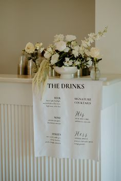 the drinks menu is hanging on a towel rack with flowers in vases next to it