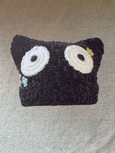 a crocheted black cat pillow with white eyes