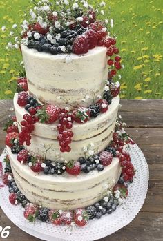 a three tiered cake with berries and flowers on the top is sitting on a wooden table