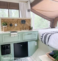 a bedroom with a bed, sink and refrigerator in it next to a window that looks out onto the woods