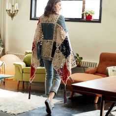 a woman walking through a living room wearing a crocheted shawl over her shoulders