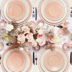 the table is set with pink and white plates, silverware, and flower centerpieces