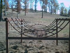 an old rusted metal bed frame sitting in the middle of a field with trees