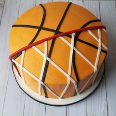 a basketball cake with white and brown icing on a wooden table next to a red ribbon