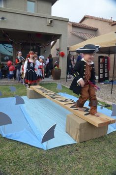 a young boy is on top of a fake ramp in front of a house with people dressed as pirates