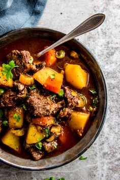 a bowl filled with stew and potatoes on top of a table next to a blue towel