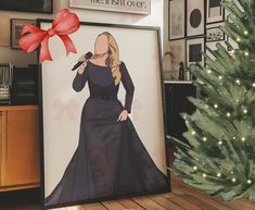 a christmas tree is next to a framed poster with a drawing of a woman in a black dress